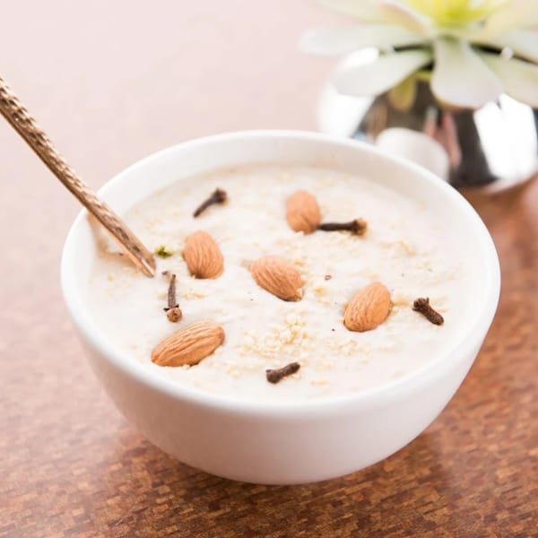 A white bowl of creamy dessert, garnished with almonds and cloves, with a spoon.