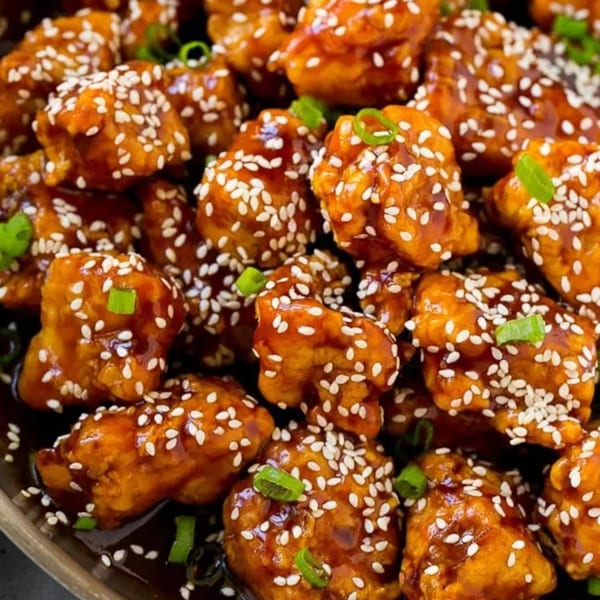 Close-up of glazed halal Chinese Indo Pak chicken bites, garnished with sesame seeds and green onions.