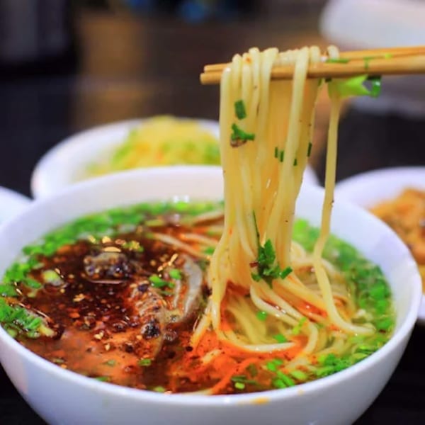 Chopsticks lifting long noodles from a bowl of spicy Halal Chinese Indo Pak soup.