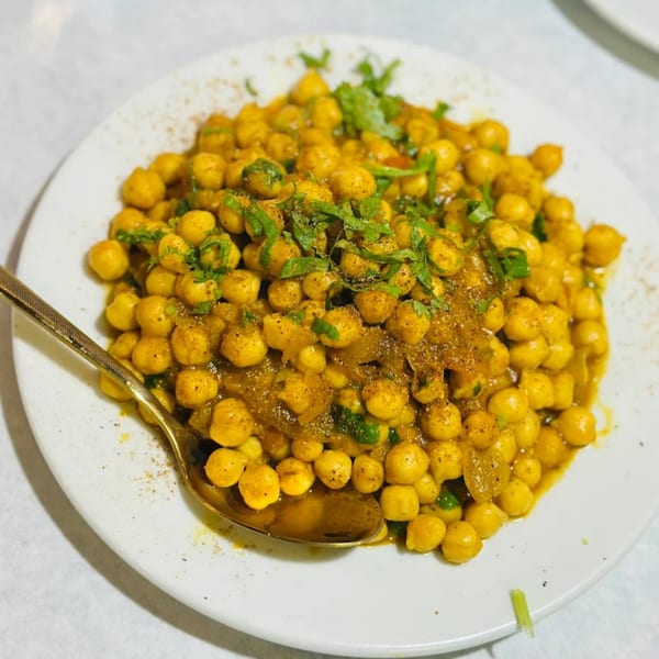 A close-up of a white plate filled with yellow chickpeas in a rich sauce, garnished with fresh herbs.