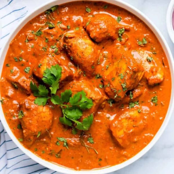 A white bowl filled with orange chicken curry, garnished with fresh green cilantro.