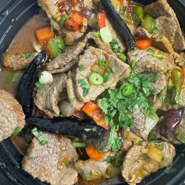 Halal Chinese Indo Pak beef dish with vegetables, chili peppers, and cilantro in a dark bowl.